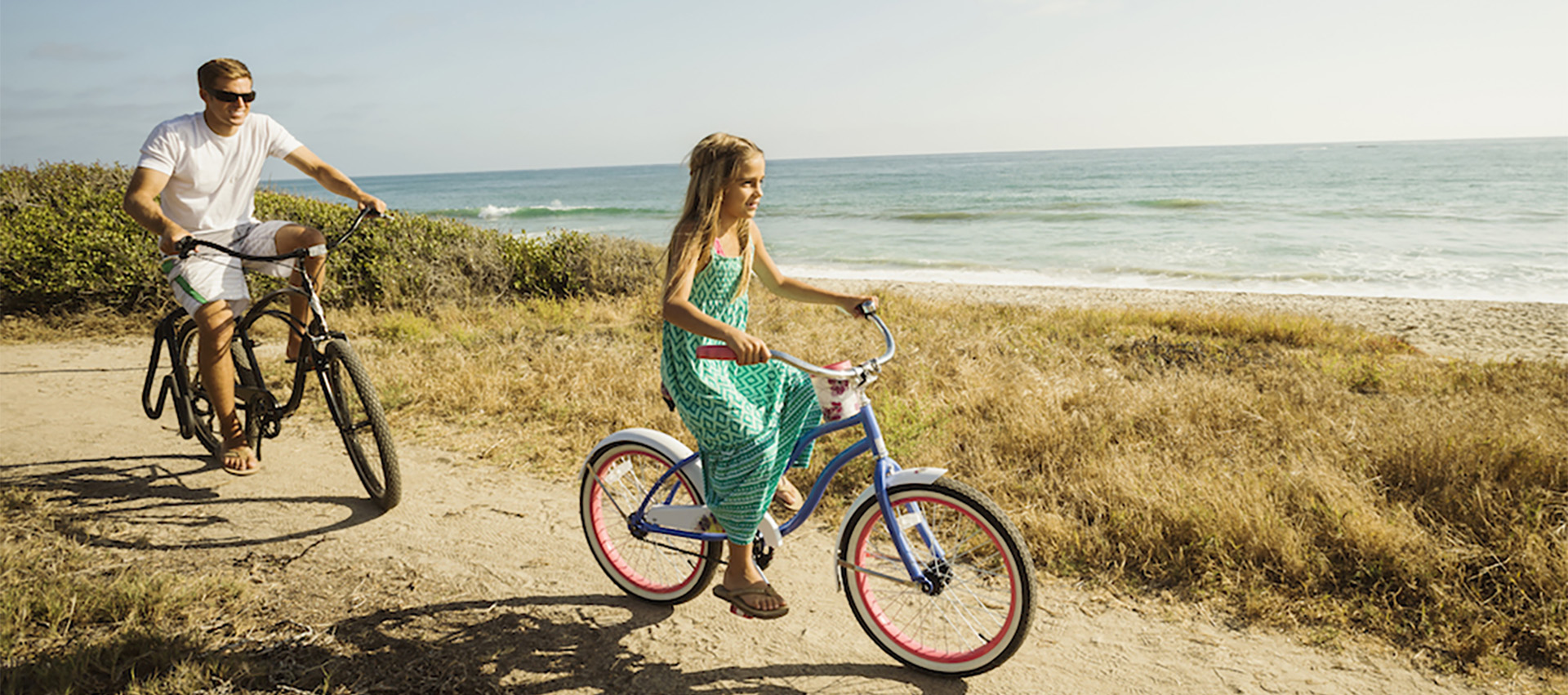 Image of a father and daughter biking along the beach